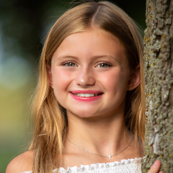 young blonde girl leaning against a tree smiling with bright smile