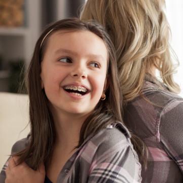 young girl with braces smiling while leaning against her mother